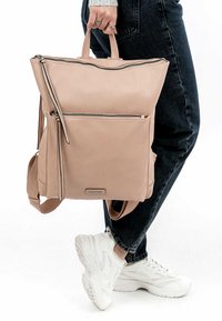 Zaino in pelle rosa chiaro con manico superiore, numerosi scomparti con zip, cuciture a contrasto e spallacci regolabili.