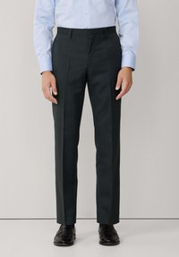 Donkergrijze op maat gemaakte broek met een zachte textuur, voorzien van een recht model, voorplooien en riemlussen, gedragen met zwarte schoenen.