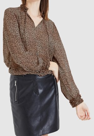 Braune Bluse aus transparentem Leopardenmuster mit rüschigem Halsausschnitt und gerafften Ärmeln, kombiniert mit einem schwarzen Minirock aus Leder mit Reißverschlusstaschen.