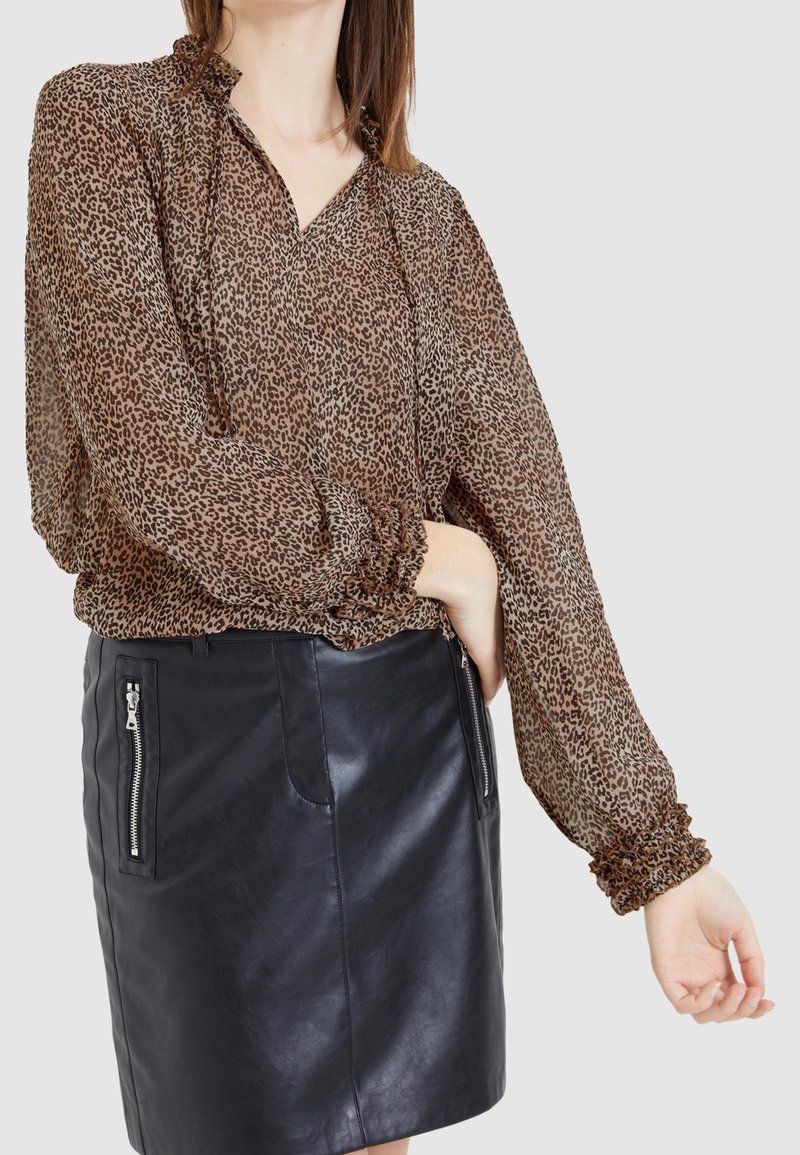 Chemisier transparent à imprimé léopard marron avec un col froncé et des manches gather, associé à une mini jupe en cuir noir avec poches zippées.