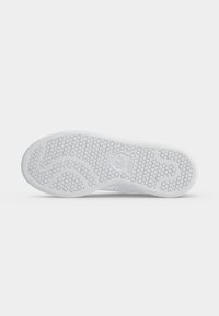 Podošva bielej tenisky Adidas s vzorom medovej plástvy a logom Adidas v strede podrážky.