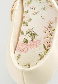 Ballerine beige chiaro con finitura liscia, dotata di soletta con motivo floreale decorato da rose rosa e foglie verdi su uno sfondo testurizzato.