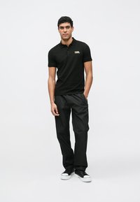 Čierne polokošeľa s logom, spárované s čiernymi cargo nohavicami. Model nosí čierne tenisky. Jednoduchý dizajn, hladká textúra, priliehavý strih.