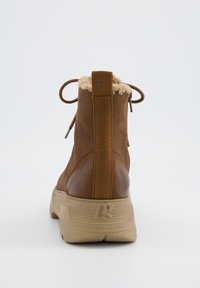 Bruine enkelboots van textuurleer, met een nepbont kraag, elastische veters en een beige rubberen zool met merkaccenten.
