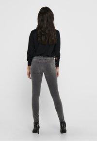 Gray skinny jeans with back pockets, made from a stretchy fabric. Paired with a black long-sleeve shirt and black heeled boots.