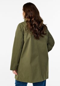 Cappotto verde oliva con una vestibilità rilassata, maniche lunghe e una texture liscia. Presenta un taglio dritto e un design minimalista.