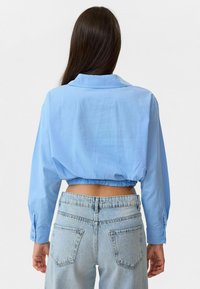 Lichtblauw cropped shirt met lange mouwen, knoopmanchetten en een kraag; geplooide zoom; gecombineerd met lichtdenim jeans.