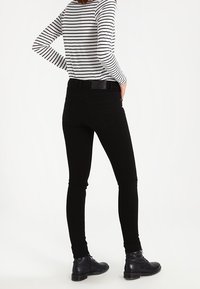 Jeans skinny negros con una textura suave, que cuentan con una cintura de altura media, bolsillos traseros y se combinan con botas negras de cordones.
