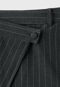 Tissu gris foncé à fines rayures avec une ceinture et une fermeture par bouton recouvert de tissu sur un vêtement portefeuille.