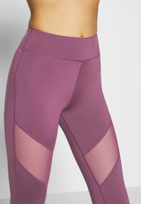 Leggings taille haute violets avec une texture lisse, des découpes en maille en motif chevron et des coutures renforcées pour plus de durabilité.