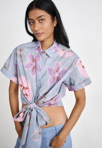 Camicia in cotone blu a maniche corte con motivo floreale in rosa e marrone, con un dettaglio di nodo sul davanti e un fit rilassato.