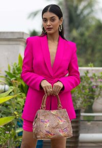 Fuchsia maßgeschneiderte Blazer mit tailliertem Schnitt, kombiniert mit einer braunen Handtasche, die farbenfrohe Kolibri-Muster und goldfarbene Hardware aufweist.