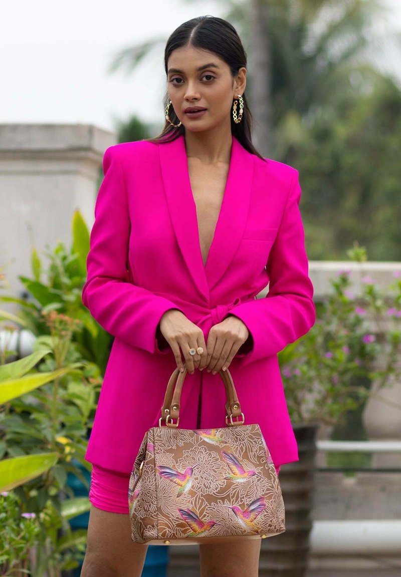 Fuchsia maßgeschneiderte Blazer mit tailliertem Schnitt, kombiniert mit einer braunen Handtasche, die farbenfrohe Kolibri-Muster und goldfarbene Hardware aufweist.