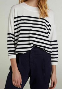 White and navy striped long-sleeve top with a wide neckline, relaxed fit, and ribbed cuffs, paired with dark pants.
