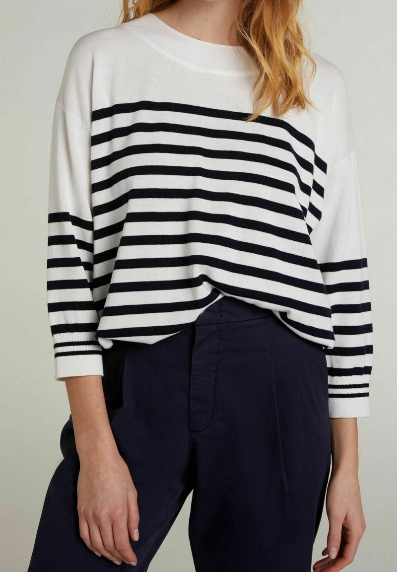 White and navy striped long-sleeve top with a wide neckline, relaxed fit, and ribbed cuffs, paired with dark pants.