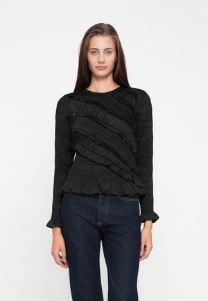 Top nero a maniche lunghe con volant sovrapposti, un motivo testurizzato e un design aderente, abbinato a jeans in denim scuro.