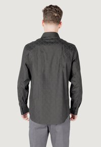 Camicia nera a maniche lunghe con motivo geometrico, polsini con bottoni e orlo curvo, vista dal retro.