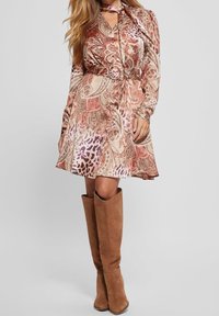 Robe marron à motif cachemire avec manches longues et taille cintrée, associée à de hautes bottes en daim marron. Texture lisse et design fluide.