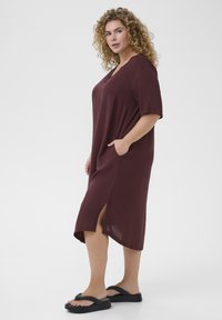 Burgundy cotton dress with wide sleeves, side pockets, and side slits. Worn with black platform sandals, featuring a smooth texture.