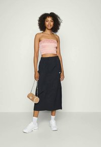 Saia preta da Nike com bolsos, top tubular pregueado rosa, ténis brancos e uma bolsa circular bege com alça de corrente. Textura suave em toda a parte.