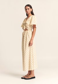 Rumena zgornji del s pikami in mašno, skrajšan ter kombiniran z dolgo ujemajočo se krilo. Model nosi japonke; ozadje je nevtralno.