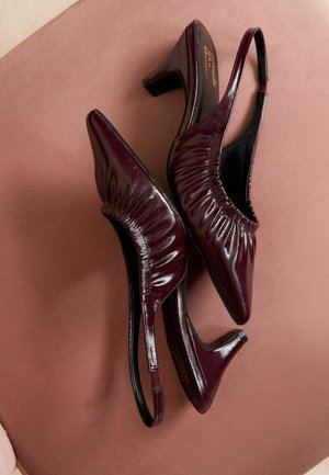 Tumši sarkani siksnu blokzābaki ar norādītu purngalu, krokotu tekstūru un mērenu bloku papēdi. Spīdīga apdare uz gludas ādas materiāla.