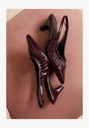 Tumši sarkani siksnu blokzābaki ar norādītu purngalu, krokotu tekstūru un mērenu bloku papēdi. Spīdīga apdare uz gludas ādas materiāla.