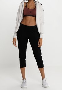 Svarta korta träningsbyxor, brun sport-bh och en ljusgrå zip-up hoodie. Materialet verkar slätt, med en åtsittande design och minimal hårdvara.