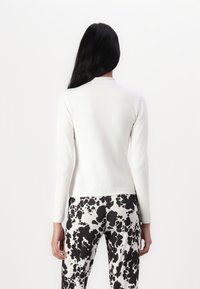 White long-sleeve top with a high neckline, paired with black-and-white patterned pants featuring an abstract splatter design.
