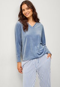 Lichtblauw velours t-shirt met lange mouwen en V-hals, gecombineerd met witte en blauwe gestreepte pyjamabroek. Zachte textuur, ontspannen pasvorm.