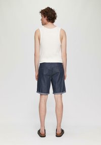 Shorts en denim usés de couleur bleu foncé avec des ourlets retroussés, associés à un débardeur de couleur claire. Le tissu a une texture lisse.
