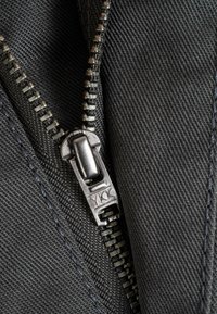 Black fabric with a textured surface, featuring a metal zipper with a silver pull tab engraved "YKK," positioned on the side.