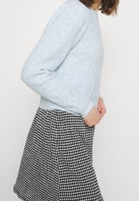 Suéter de punto acanalado azul claro con mangas largas, combinado con una falda de patrón de pata de gallo en blanco y negro. Textura suave y diseño ajustado.