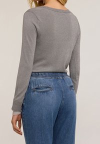 Pull gris à manches longues avec un col rond et une finition métallique. Associé à un jean en denim bleu avec une taille élastique et des poches arrière.