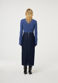 Blauw gebreid topje met textuur, gecombineerd met een donkere denim maxi rok, voorzien van een rits aan de achterkant en een zijsplit, aangevuld met zwarte enkellaarsjes.