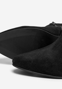Stivaletti neri in suede con punta affusolata, suola piatta in gomma con superficie texture e zip laterale per la chiusura.
