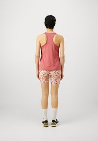 Canotta sportiva rossa con design a schiena scoperta, abbinata a pantaloni corti a fantasia floreale in crema e rosa, e scarpe da ginnastica nere con calzini bianchi.