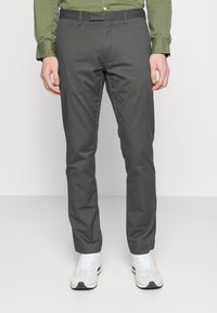 Graue, schlank geschnittene Hose aus glattem Stoff, mit einem klassischen Bund und vorderen Taschen, kombiniert mit weißen und grauen Sportschuhen.