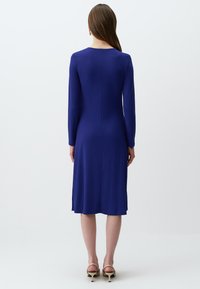 Langärmliges Kleid in lebhaftem Blau mit glatter Textur, das knapp unter das Knie fällt, mit einem Rundhalsausschnitt und schlichten Designelementen.