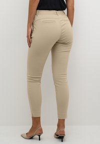Pantaloni beige aderenti con una texture liscia, gambe affusolate e tasche posteriori. Indossati con scarpe con tacco di colore chiaro.