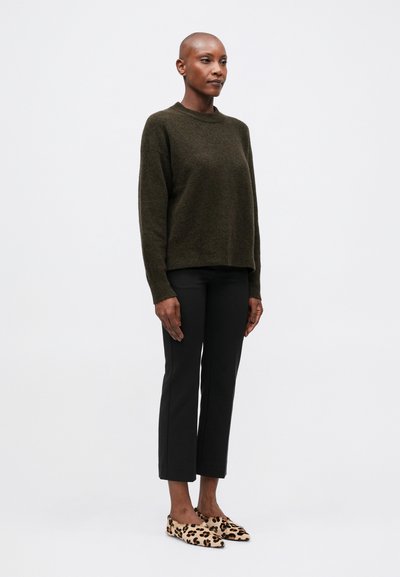 Sweater de lã verde-escuro, calças pretas ajustadas e sapatos slip-on bege com padrão de leopardo. Corte simples e relaxado com decote e punhos canelados.