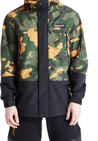 Kamouflagejacka i grön och orange, med en svart nederdel, utrustad med huva, dragkedjestängning och Timberland-logotyp på bröstet.