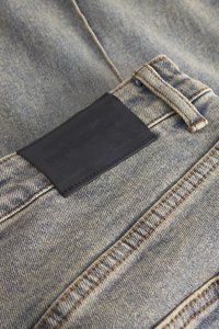 Denim jeans med en lys blå vask, med en svart lærpatch med preget tekst på linningen og kontrastfarget oransje søm.