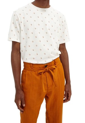 White cotton t-shirt with repeated orange diamond patterns, paired with orange striped trousers featuring a tied waist and a single button.