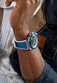 Blaues Chronographen-Armbanduhr mit einem Silber- und Goldgehäuse, blauen strukturierten Silikonarmband und einem weißen Zifferblatt mit goldenen Akzenten und Subzifferblättern.