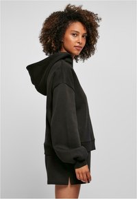 Sudadera negra corta con mangas anchas y una capucha grande, combinada con pantalones cortos a juego. Textura suave, detalles mínimos, ajuste casual.