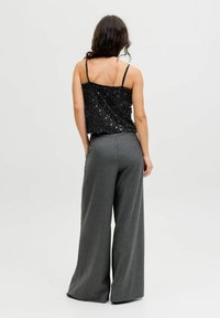 Melna pērļu tops ar plānām siksniņām, kombinēts ar platajiem pelēkajiem biksēm, kuru rakstā ir tekstūra un piedāvā pielāgotu siluetu.