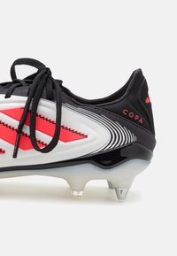 Black and white soccer cleat with red accents, featuring a textured design, lace-up closure, and a translucent sole with pointed studs.