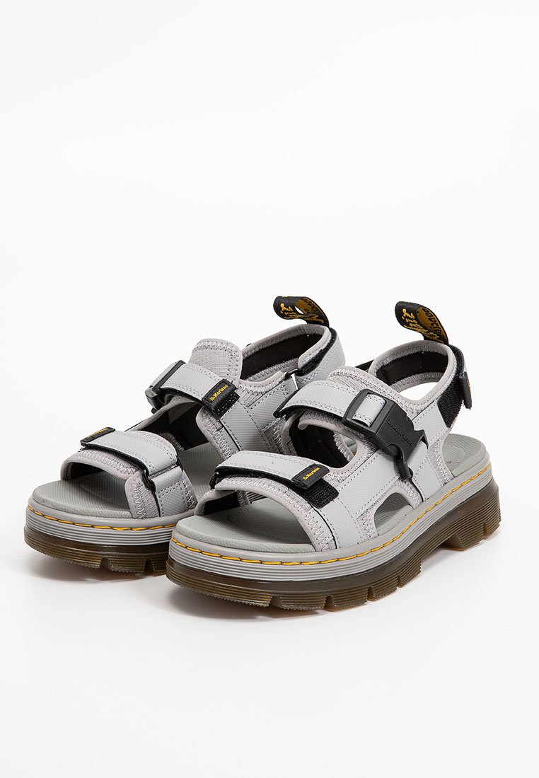 Graue Sandalen mit einem strukturierten Obermaterial, verstellbaren Riemen in Schwarz und einer dicke Gummisohle mit gelben Nähten und einem transparenten Profil.