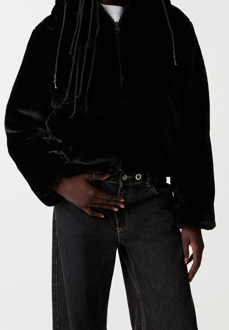 Black faux-fur zip-up jacket with a hood, featuring a relaxed fit and soft texture, paired with dark denim jeans and a white shirt.